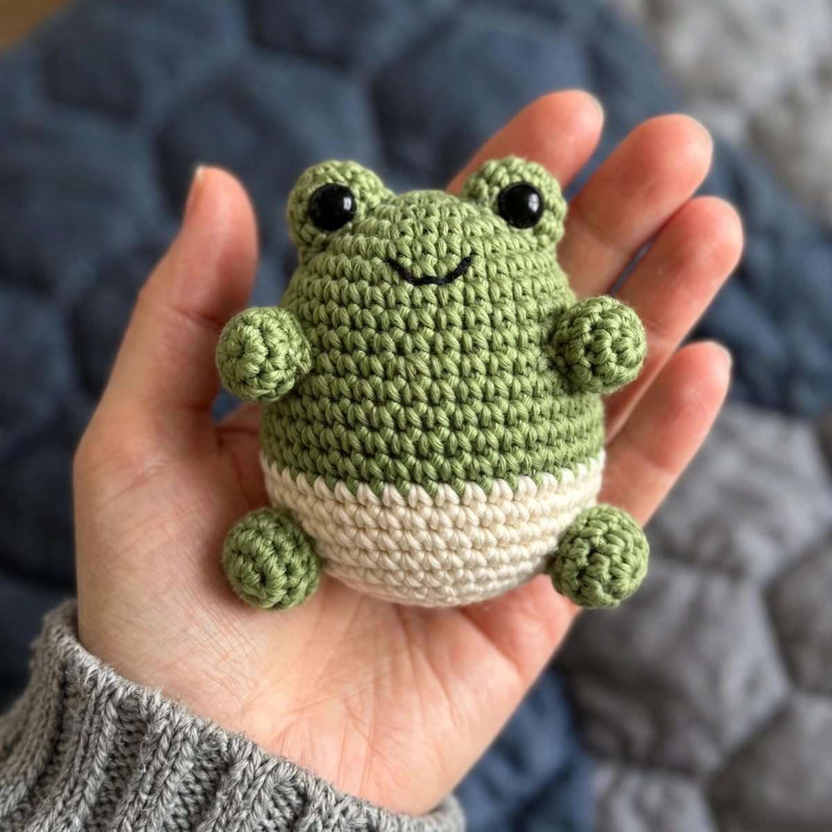 Green crochet mini sitting frog amigurumi with a cream belly held in a hand